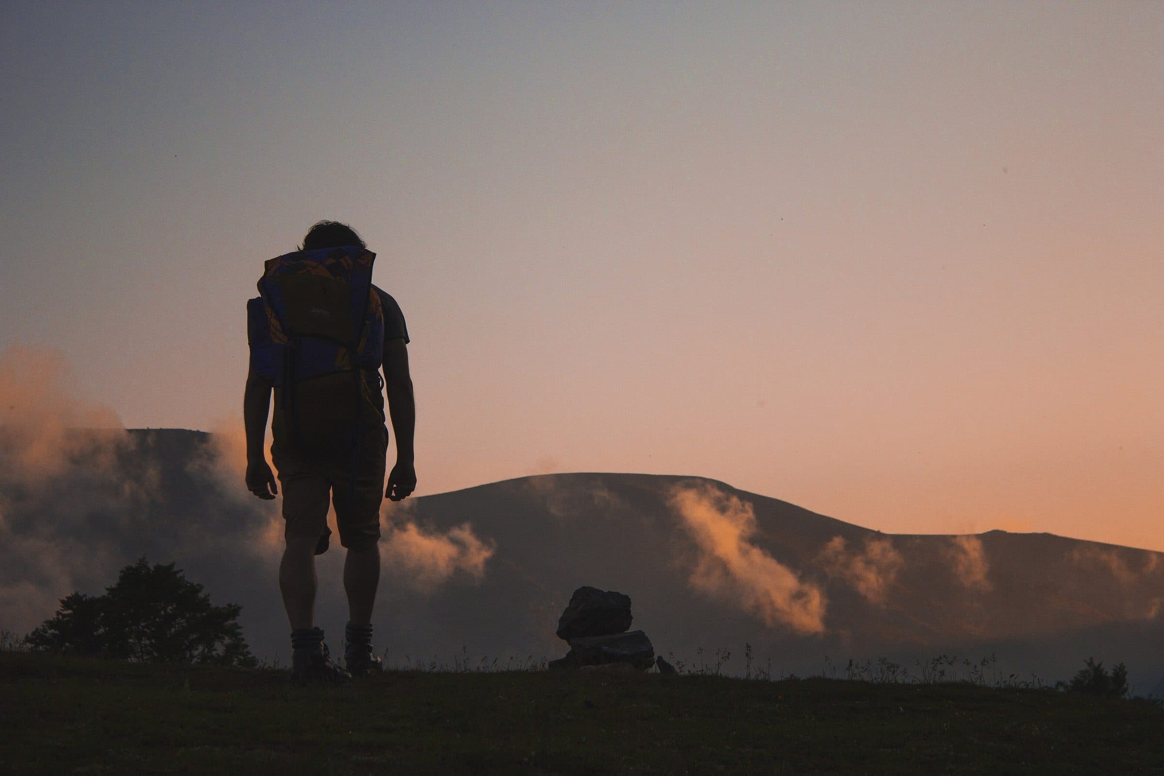 A hiker in silhouette walking a ridge at dusk