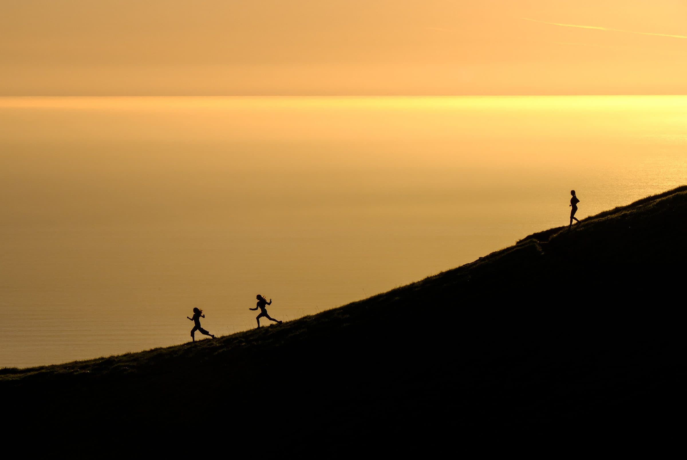 Three runners in silhouette on a ridge at dusk
